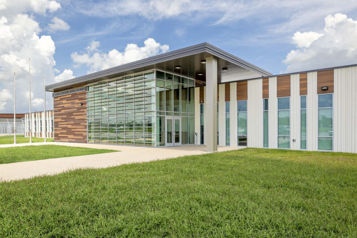 Louisiana Correctional Institute building with glass entry, mixed material exterior, and open green space creating a bright, accessible community space.